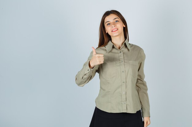 Young lady in shirt, skirt showing thumb up and looking happy , front view.