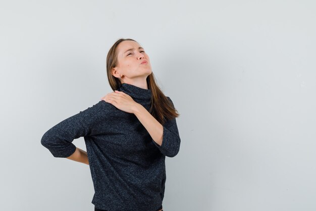 Young lady in shirt suffering from backache and looking fatigued