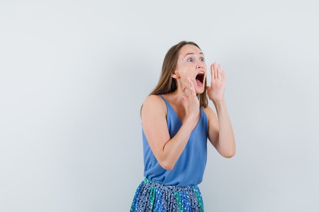 Young lady shouting or announcing something in singlet, skirt and looking excited , front view.