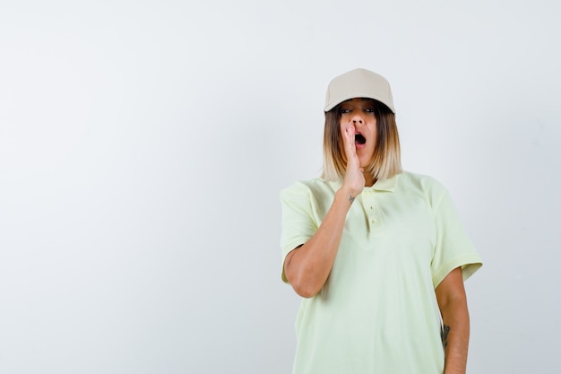 Young lady shouting something in t-shirt, cap and looking serious , front view.