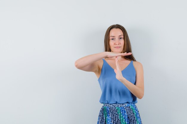 Young lady showing break up gesture in blue blouse,skirt and looking serious. front view.