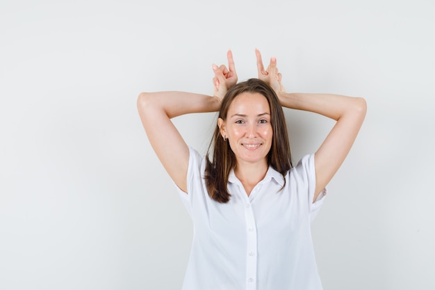 Young lady showing bunny gesture in white blouse and looking funny