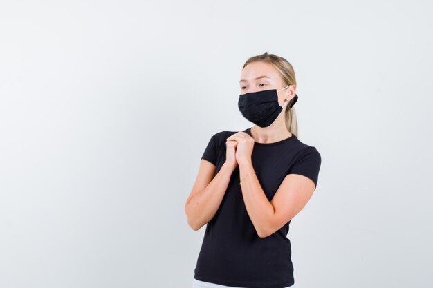 Young lady showing clasped hands in pleading gesture in t-shirt