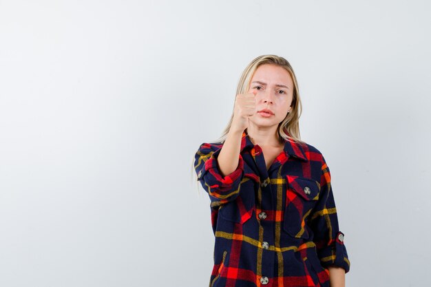 Young lady showing clenched fist in checked shirt and looking serious , front view.