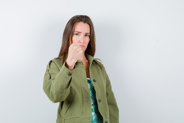 Young lady showing clenched fist in green jacket and looking proud , front view.