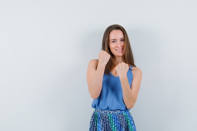 Young lady showing clenched fists in singlet, skirt and looking confident