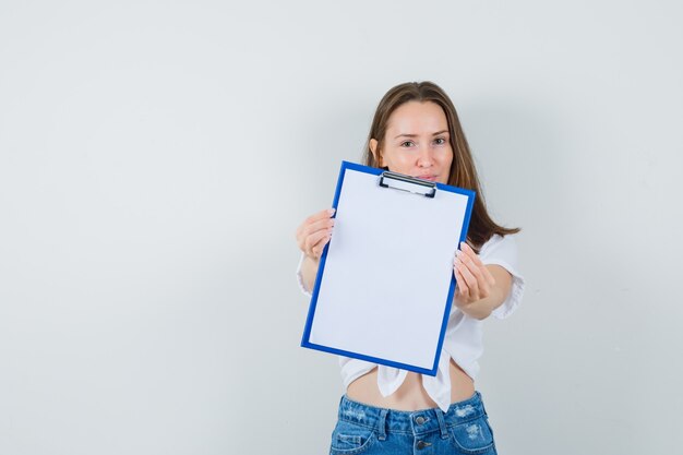 Young lady showing clipboard in white blouse and looking focused. front view.