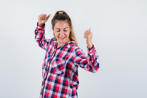 Young lady showing double thumbs up in checked shirt and looking happy. front view.