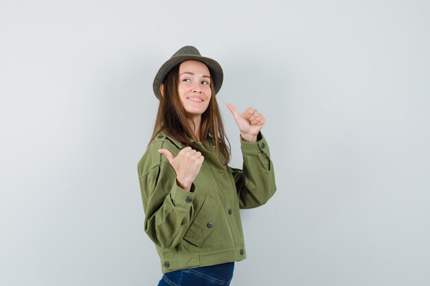 ジャケットのズボンの帽子で二重の親指を示し、陽気に見える若い女性
