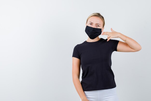 分離されたTシャツ、ズボン、医療マスクで銃のジェスチャーを示す若い女性