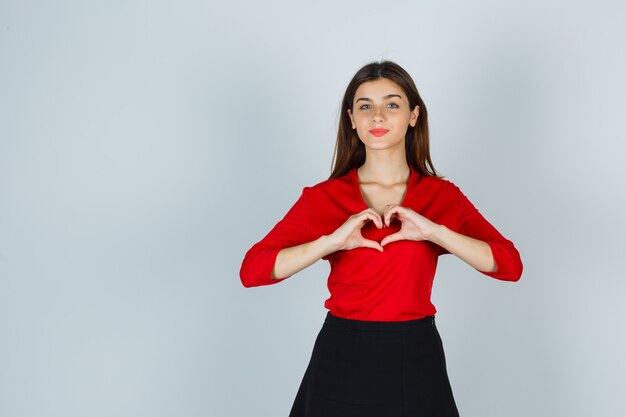 Young lady showing heart gesture in red blouse, skirt and looking gorgeous