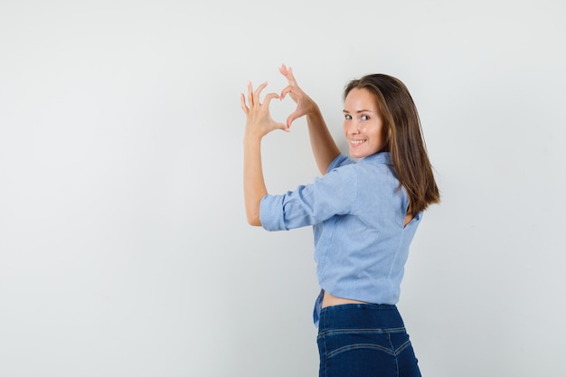 Young lady showing heart gesture and smiling in blue shirt