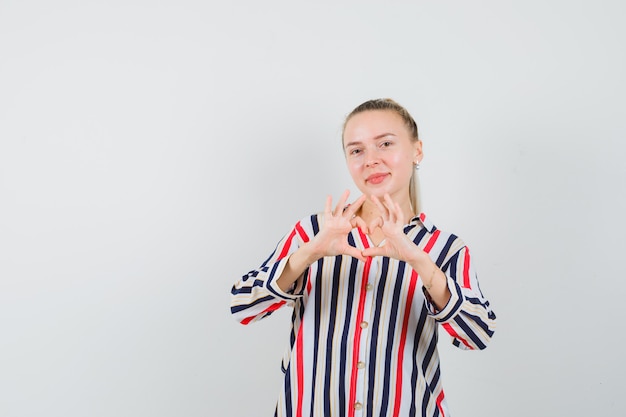Free photo young lady showing heart gesture in striped shirt and looking cheerful