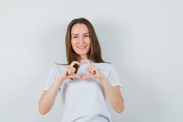 Young lady showing heart gesture in white t-shirt and looking cheery  