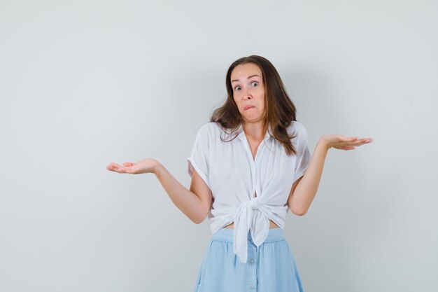 Young lady showing helpless gesture in blouse, skirt and looking troubled