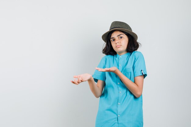 Young lady showing helpless gesture in blue shirt, hat and looking lost.