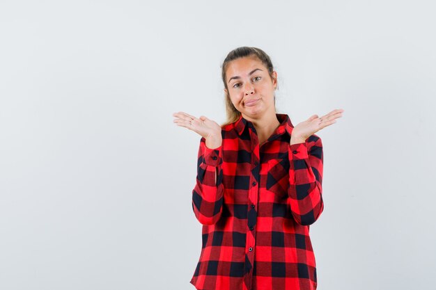 Young lady showing helpless gesture in casual shirt and looking confused , front view.