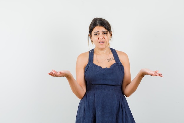 Young lady showing helpless gesture in dress and looking puzzled