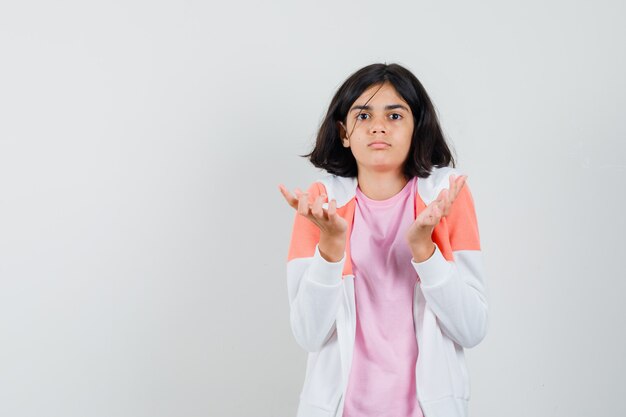 Young lady showing helpless gesture in jacket, pink shirt and looking puzzled.