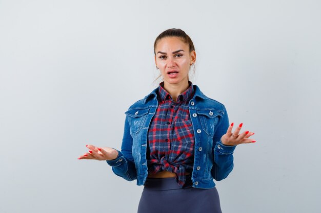 Young lady showing helpless gesture in shirt, jacket and looking puzzled. front view.