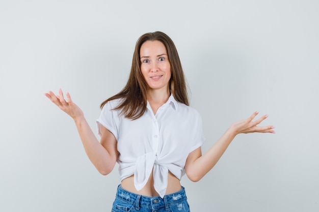 Young lady showing helpless gesture in white blouse front view.