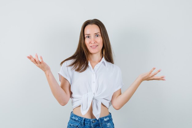 Young lady showing helpless gesture in white blouse front view.