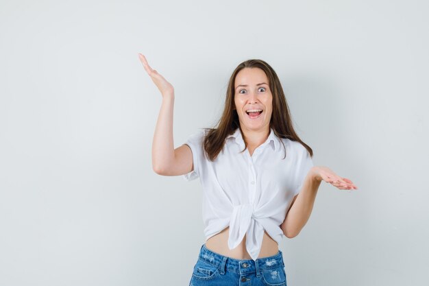 Young lady showing helpless gesture in white blouse and looking funny , front view.