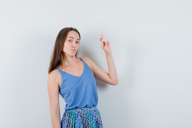 Young lady showing her crossed fingers in blue blouse,skirt and looking confident , front view.