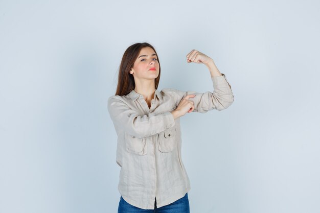 Young lady showing her muscles in casual, jeans and looking confident , front view.