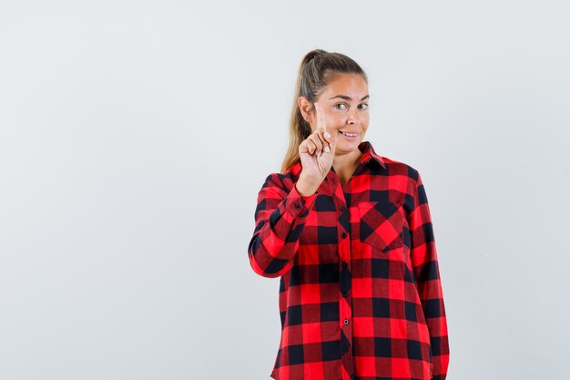 Young lady showing hold on a minute gesture with finger up in casual shirt and looking confident , front view.