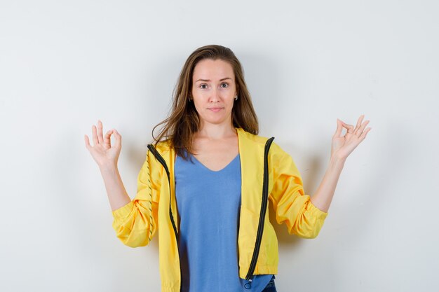 Young lady showing meditation gesture in t-shirt, jacket and looking confident, front view.