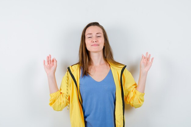 Молодая дама показывает жест медитации в футболке и выглядит расслабленным. передний план.