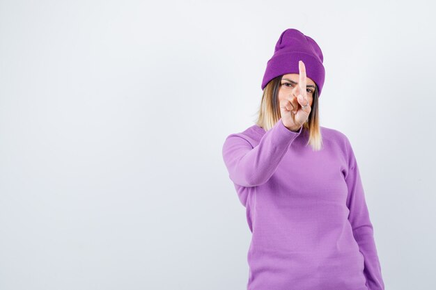 Юная леди демонстрирует минутный жест в фиолетовом свитере, шапочке и выглядит уверенно. передний план.
