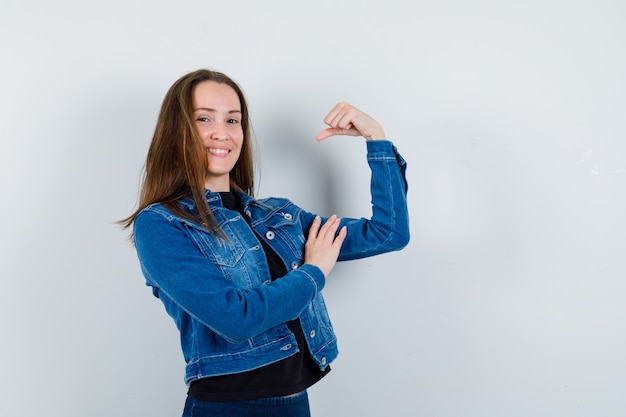 Young lady showing muscles of arm in blouse, jacket and looking confident, front view.