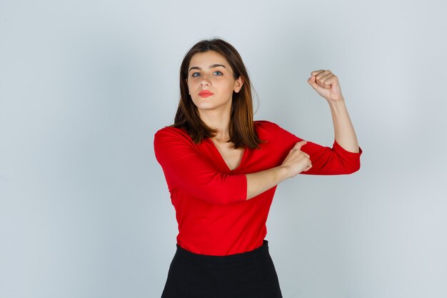 Young lady showing muscles of arm in red blouse, skirt and looking confident