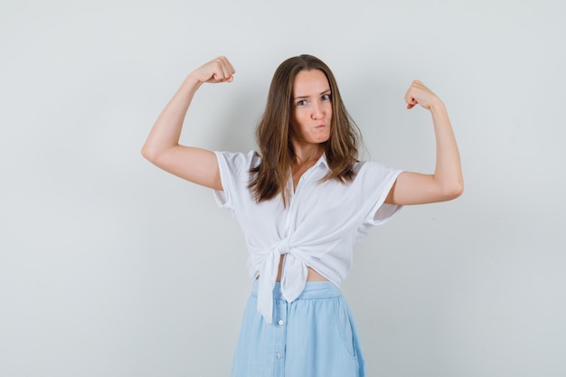 Young lady showing muscles of arms in blouse and skirt and looking confident