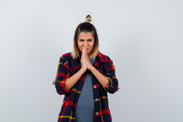 Young lady showing namaste gesture in casual checked shirt and looking attractive , front view.