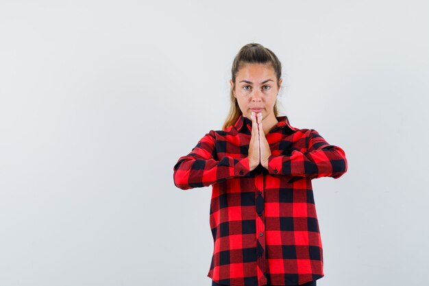 Young lady showing namaste gesture in checked shirt and looking confident