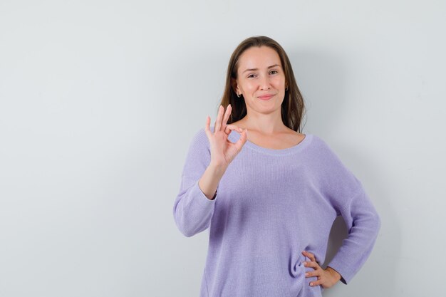 Young lady showing ok gesture in casual shirt and looking confident. front view.