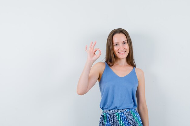 Young lady showing ok gesture in singlet, skirt and looking confident , front view.