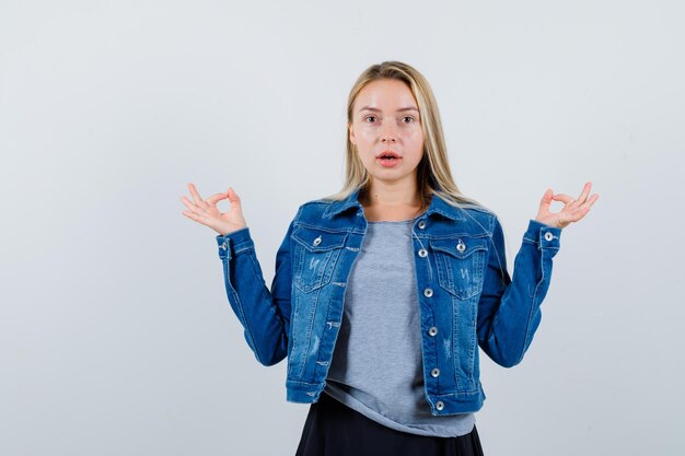 Tシャツ、デニムジャケット、スカートで大丈夫なジェスチャーを示し、驚いて見える若い女性。