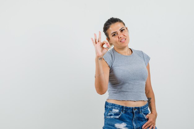 Young lady showing ok gesture in t-shirt, shorts and looking confident