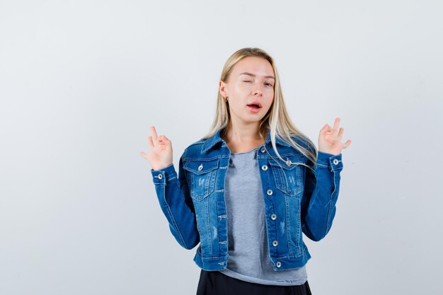 Young lady showing ok gesture while blinking in t-shirt, denim jacket, skirt and looking joyful