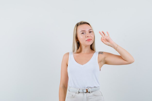 Young lady showing ok gesture in white blouse and looking delightful