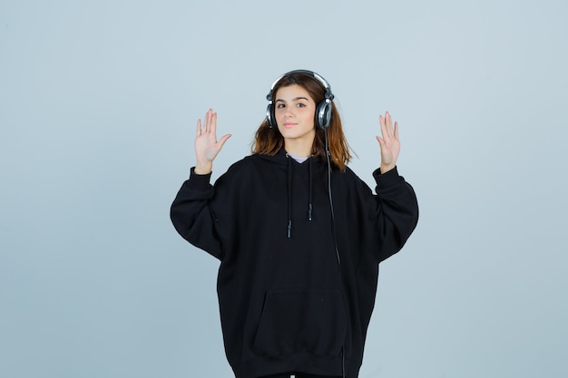 Young lady showing palms in oversized hoodie, pants and looking charming , front view.