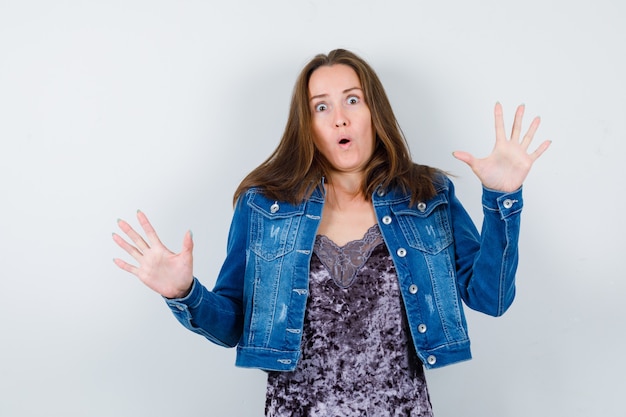 Free photo young lady showing palms in surrender gesture in blouse, denim jacket and looking puzzled. front view.