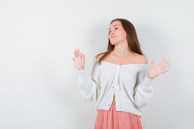 Young lady showing palms in surrender gesture in cardigan isolated