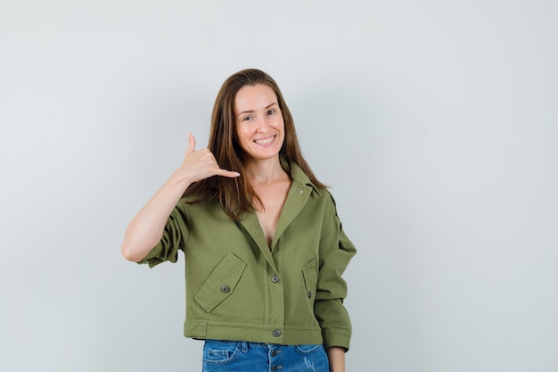 Young lady showing phone gesture in green jacket shorts and looking merry 