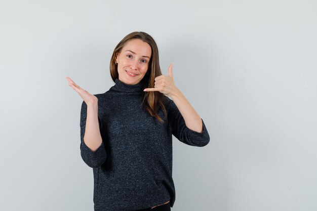 Young lady showing phone gesture in shirt and looking confident