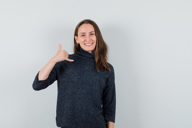 Young lady showing phone gesture in shirt and looking positive